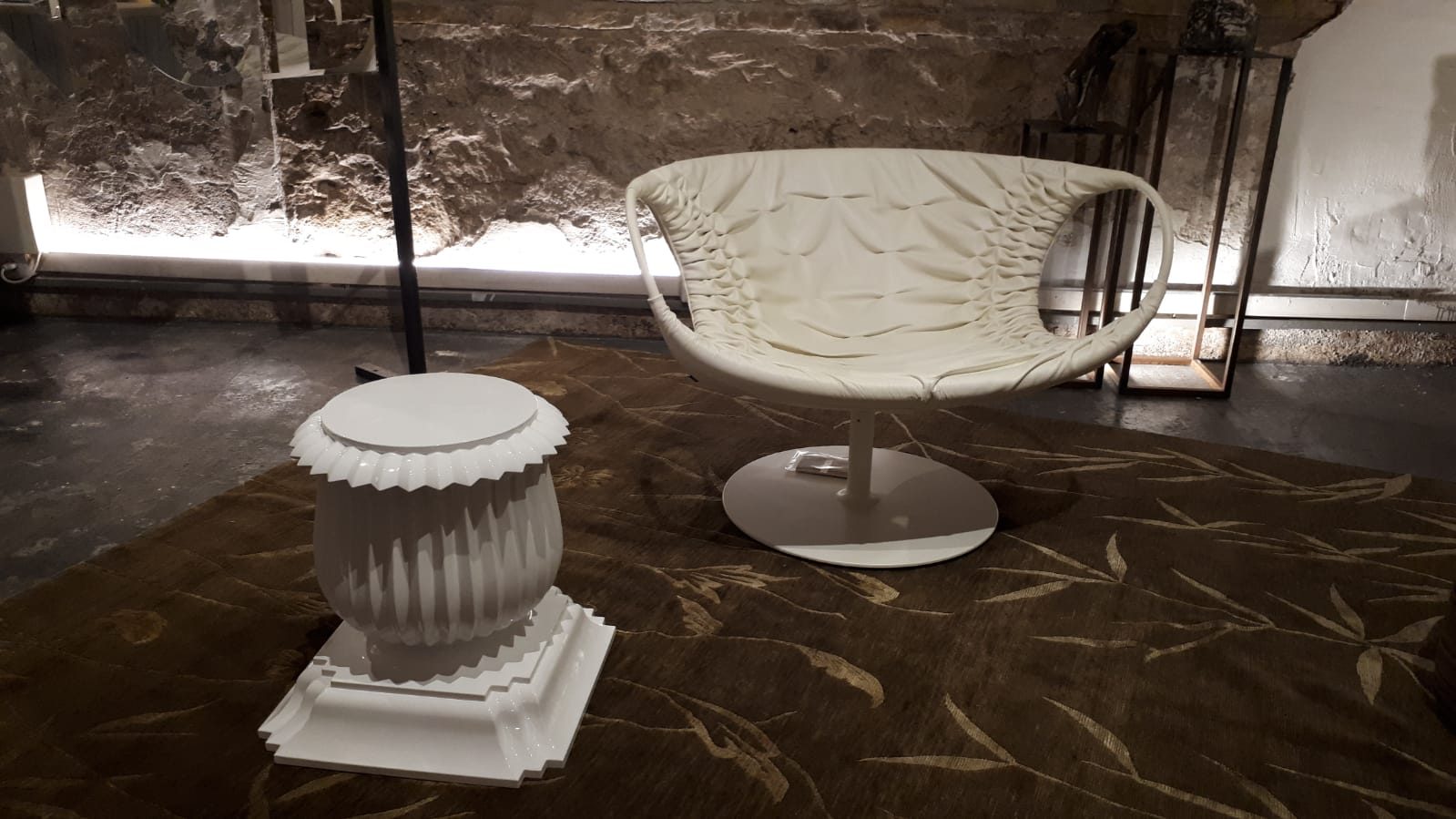 Poltrona bianca e tavolino scultoreo su muro in pietra a vista, nello showroom Bistolfi