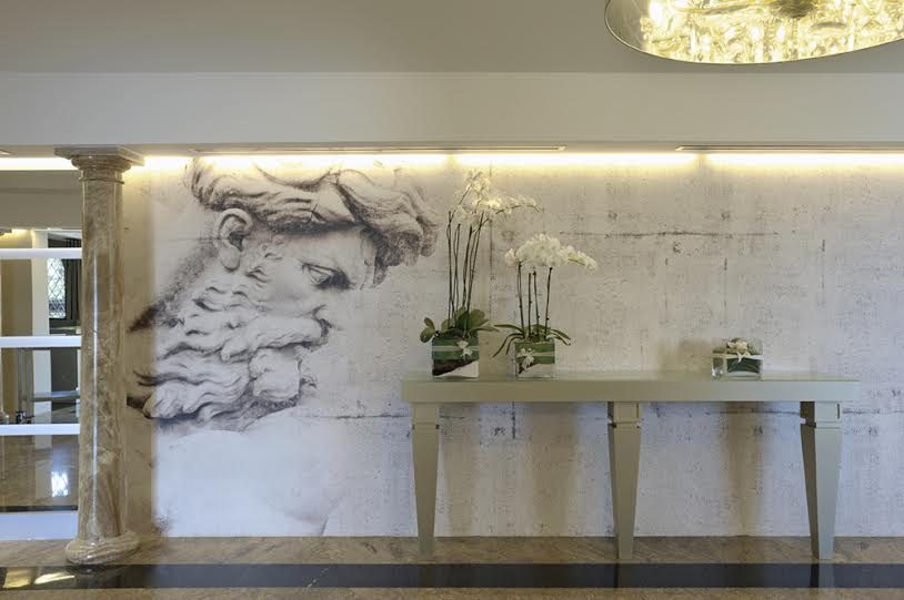 Parete con un grande volto barbuto disegnato in stile michelangiolesco, una consolle chiara e orchidee bianche