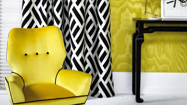 Poltrona gialla accanto a un tendaggio a fantasia geometrica in bianco e nero